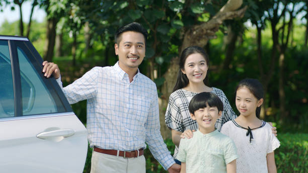 istock Asian family standing beside car, looking forward and smiling 891858910