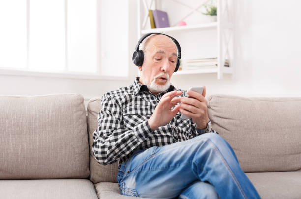 Senior man listening to music with headphones Senior man listening to music on smartphone with headphones, sitting on sofa at home, copy space old person listening to radio stock pictures, royalty-free photos & images