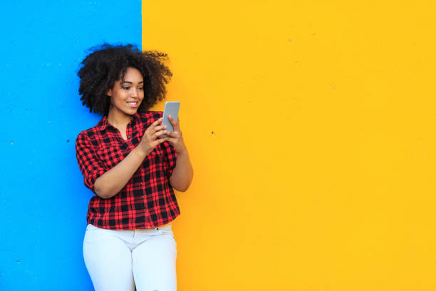 sonriente mujer americana africana escuchar música en el teléfono inteligente - colores fotos fotografías e imágenes de stock
