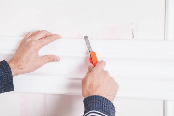 istock Man with knife cutting ceiling skirting. 891940510