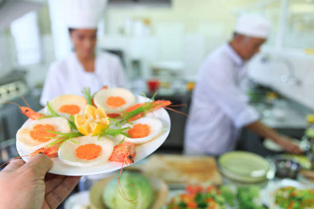 Chef preparing and presenting asian food in restaurant's kitchen.