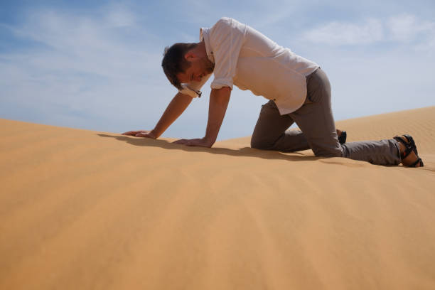 Man walking alone in the sunny desert. He is lost and out of breath. No water and energy. stock photo