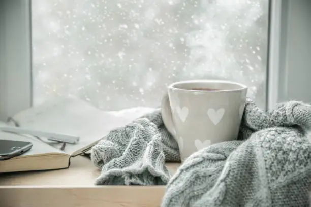 Winter cozy hot chocolate in front of window, snow, sweater. Lazy weekend, love, comfort