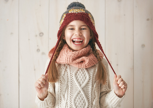 Winter portrait of happy little girl wearing knitted hat, scarf and sweater. Child on white wooden background. Fashion concept.