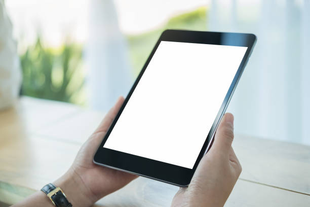istock Mockup image of hands holding black tablet pc with blank white screen on wooden table in cafe 891991694