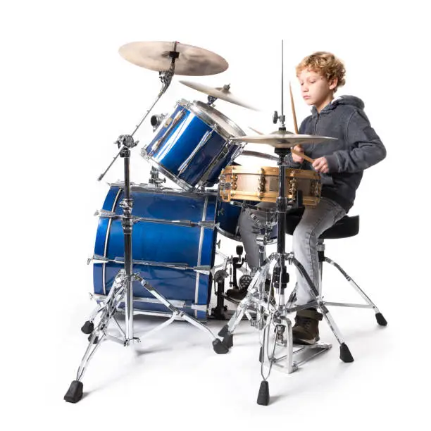 young blond caucasian boy at plays drums in studio against white background