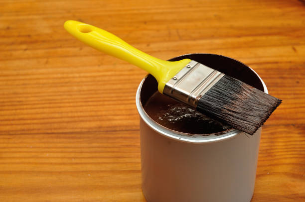 istock A white plastic container filled with brown paint and a yellow paintbrush 892028770