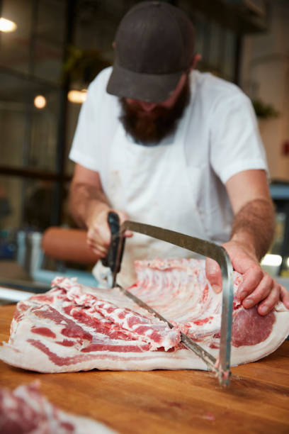 Young butcher sawing meat at a butcher's shop, vertical