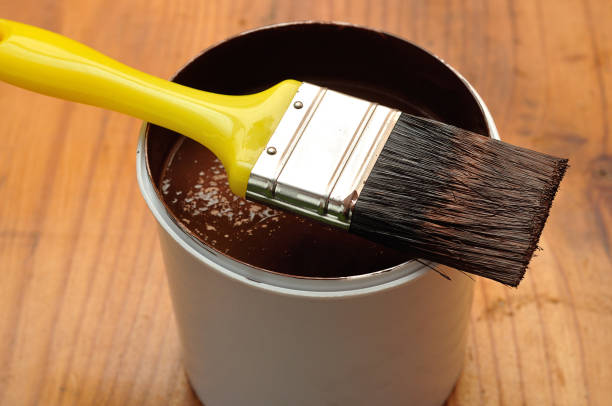 istock A white plastic container filled with brown paint and a yellow paintbrush 892031970