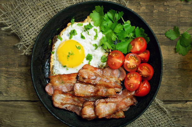 istock Fried egg with bacon, tomatoes and parsley in frying pan 892045836