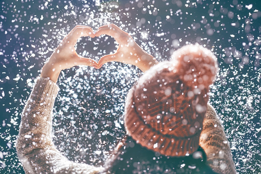 Happy young woman making hands heart on snowy winter walk in nature. Concept of frost winter season.