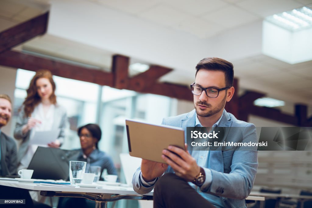 Young businessman using digital tablet and analyzing business report. Portrait of young pensive  businessman sitting at the office analyzing business report using digital tablet. Digital Display Stock Photo