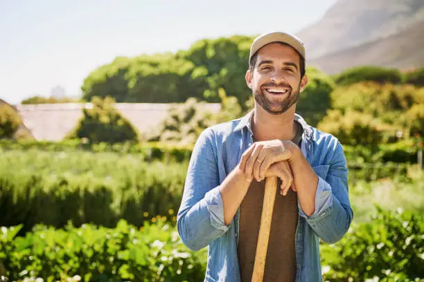 Portrait of a happy young farmer holding a spade while posing in the fields on his farm