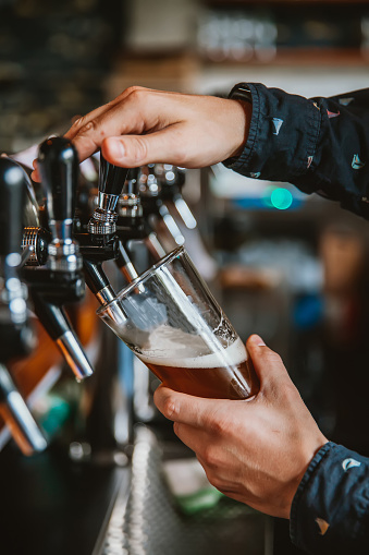 A bartender is pouring beer from tap.