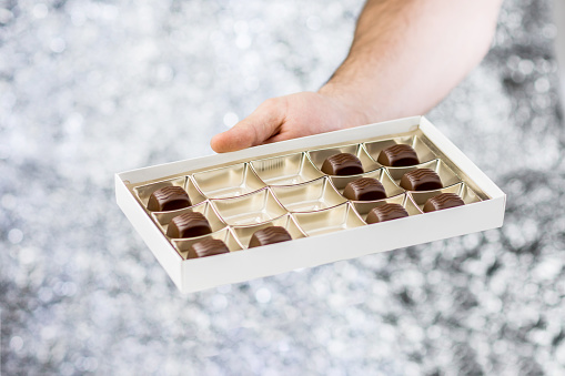 Hand Holding A Box Of Chocolates On Blurred Background With Bokeh