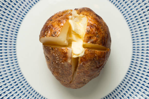 papa al horno en rodajas abierto lleno de derretir la mantequilla. - patata al horno fotografías e imágenes de stock