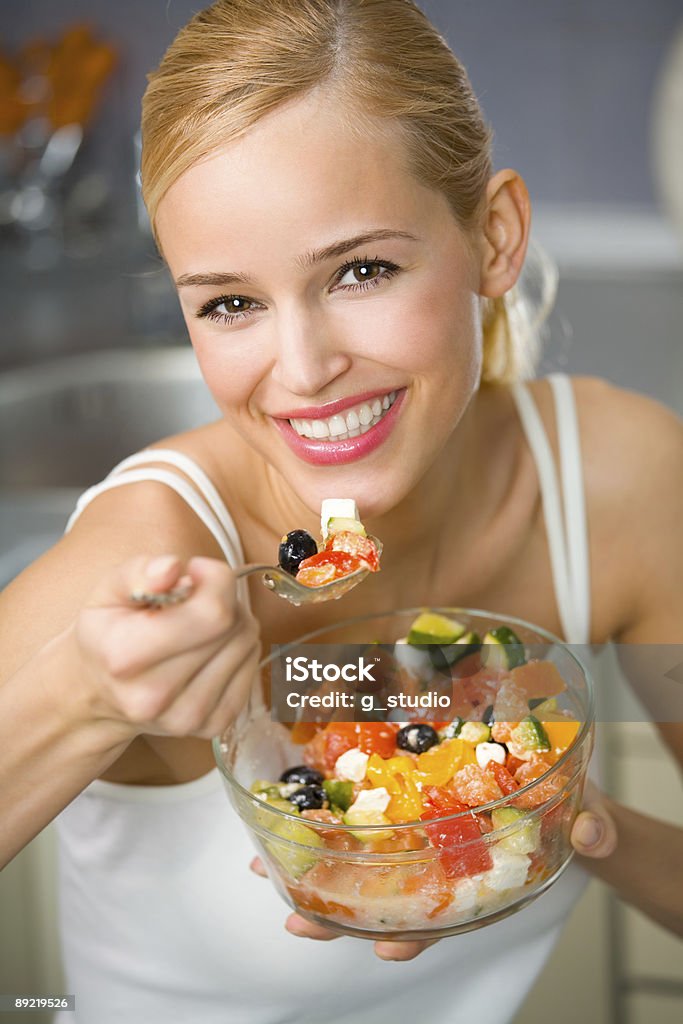 Young healthy woman eating salad in the kitchen Portrait of young happy woman eating salad at domestic kitchen Adult Stock Photo