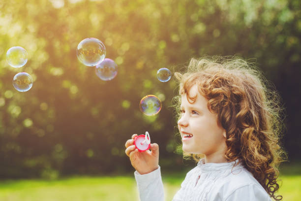 istock Little girl blowing soap bubbles in summer park. 892203780