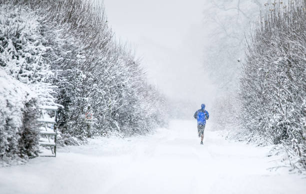 läufer unter winterlichen dezember joggen durch schneefall in cirencester park, the cotswolds - snow park road cold stock-fotos und bilder