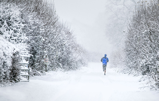 Runner taking a wintry December jog through heavy snow in Cirencester Park, The Cotswolds