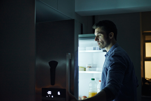 Shot of a young man opening the fridge at night in her home