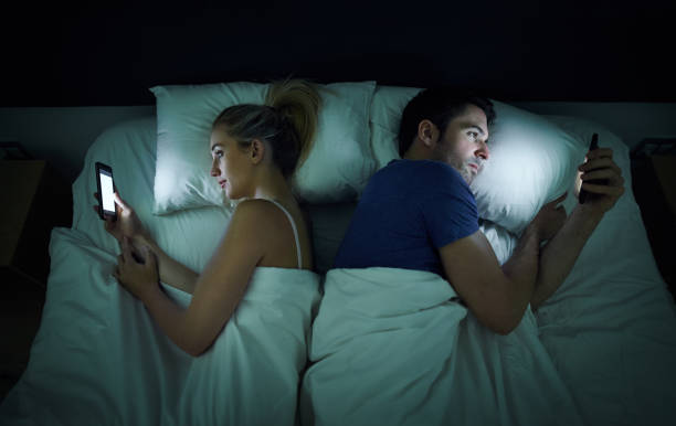 Bad bedroom etiquette Shot of a young couple using their cellphones in bed at night back to back hooked on stock pictures, royalty-free photos & images
