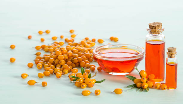 el espino amarillo y dos botellas, tazón de fuente con aceite de espino cerval de mar en la tabla azul - sea buckthorn fotografías e imágenes de stock