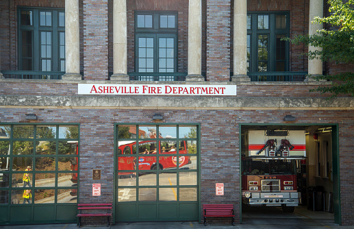 Asheville, NC, USA. September 27, 2017.  The Asheville Fire Department building with firetruck in the garage and a tourist trolley reflected in the windows.  People are riding on the trolley