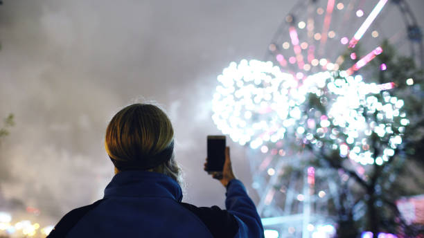 istock Closeup silhouette of man watching and photographing fireworks explode on smartphone camera outdoors 892272658