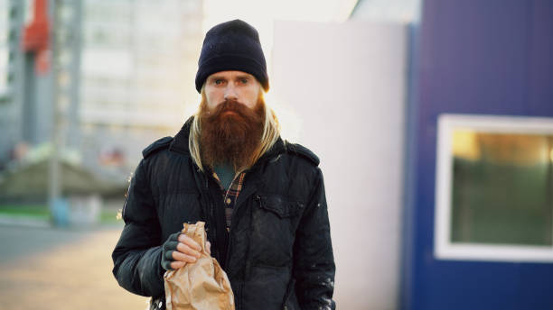 Portrait of Drunk homeless man with drink alcohol from paper bag while standing on the city street and looking at camera Drunk homeless man with drink alcohol from paper bag while standing at city street alcoholism alcohol addiction drunk stock pictures, royalty-free photos & images