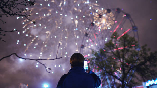 istock Closeup silhouette of man watching and photographing fireworks explode on smartphone camera outdoors 892294766