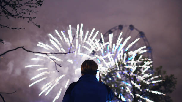 istock Closeup silhouette of man watching and photographing fireworks explode on smartphone camera outdoors 892294822
