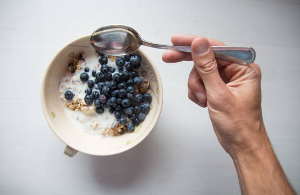 istock Hand with spoon reaching for breakfast cereal with blueberries and milk 892308624