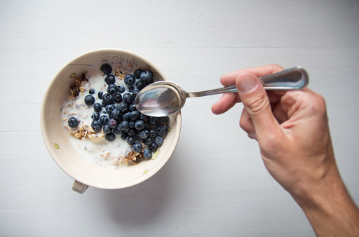 Hand with spoon reaching for breakfast cereal with blueberries and milk