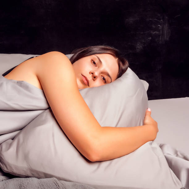 istock Woman lying in bed on a dark background with open eyes. 892338508