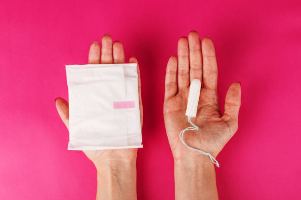 женщина, держащая менструальный тампон на розовом фоне. время менструации. гигиена и защита - padding стоковые фото и изображения
