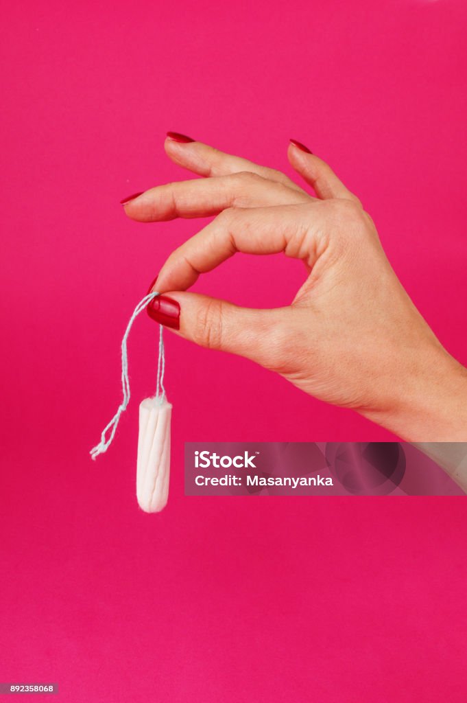Woman holding menstrual tampon on a pink background. Menstruation time. Hygiene and protection Woman holding menstrual tampon on a pink background. Menstruation time. Hygiene and protection. Adult Stock Photo