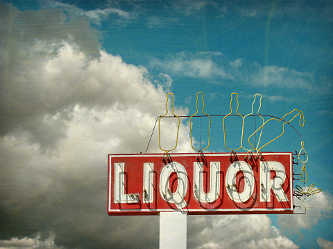 aged and worn liquor store sign with clouds