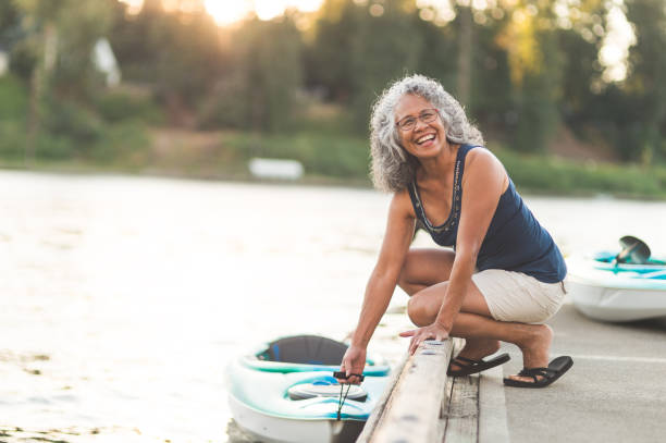 a beautiful ethnic older woman prepares to go kayaking - senior adult relaxation exercise healthy lifestyle exercising imagens e fotografias de stock