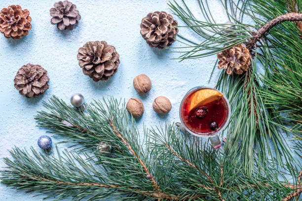 istock Hot mulled wine with orange, anise, cardamon and cinnamon on blue background. Christmas tree branches, gifts and cones 892478094