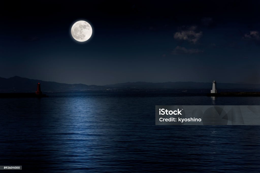 Full moon rising over the sea and the lighthouse Full moon rising over the sea and the lighthouse with copy space. Moon Stock Photo