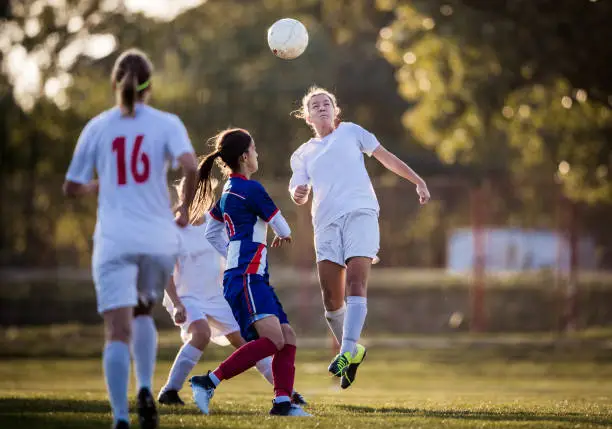 Teenage soccer player feeling determined after heading the ball before her opponent on a playing field.