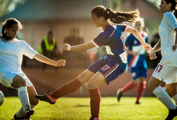 Female soccer player feeling determined after kicking the ball between opponent players during a match on playing field.