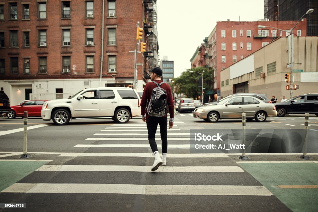 Looks like it's all clear to walk Rearview shot of a confident young man wearing a hat and walking with his backpack in the busy streets of a city Walking Stock Photo