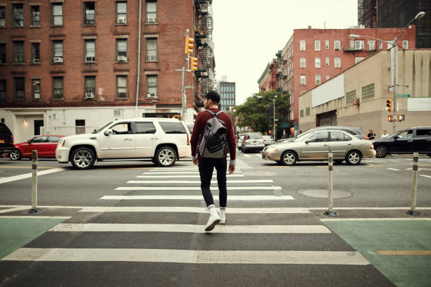 Looks like it's all clear to walk Rearview shot of a confident young man wearing a hat and walking with his backpack in the busy streets of a city man standing on sidewalk in city stock pictures, royalty-free photos & images