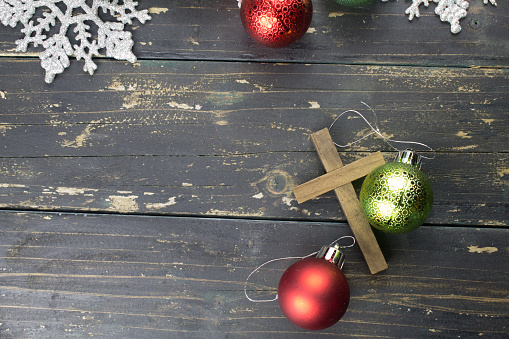 Christmas holiday ornaments and a Christian cross on a dark vintage wood background.