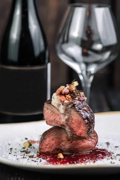 Tenderloin steak on irregular shape plate with wineglass and bottle of wine and wineglass on dark background