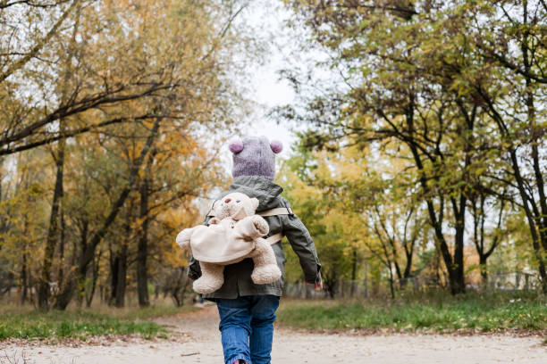 istock Little girl in autumn forest with teddy bear backpack. 892662760