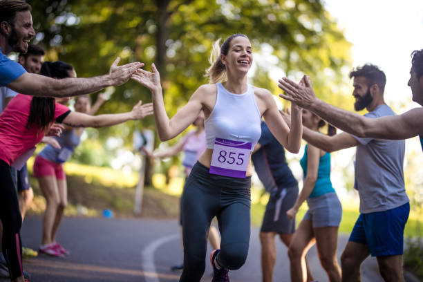 マラソンを仕上げ、挨拶の支持者のグループと若い女性。 - marathon running group of people jogging ストックフォトと画像