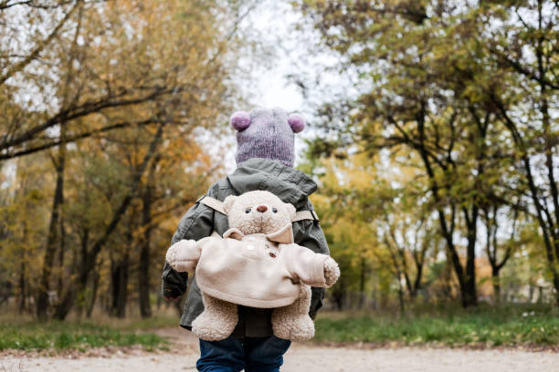 istock Little girl in autumn forest with teddy bear backpack. 892668028